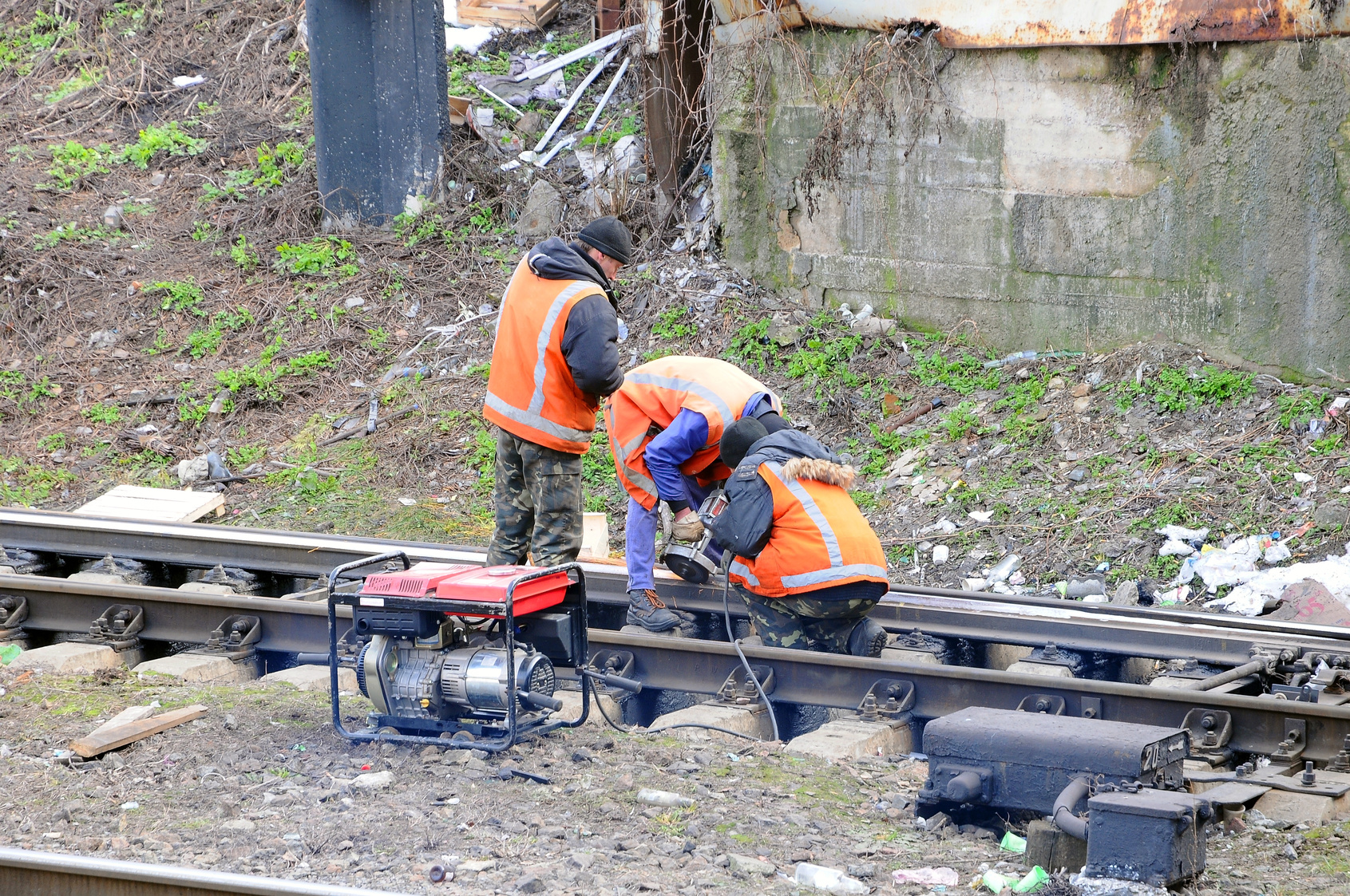 Workers grind the rails on the railroad with the help of grinders connected to the portable generator. Workers repairing the railroad.